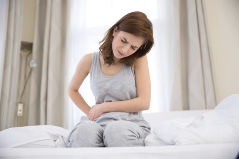 Young woman sitting on the bed with pain in stomach